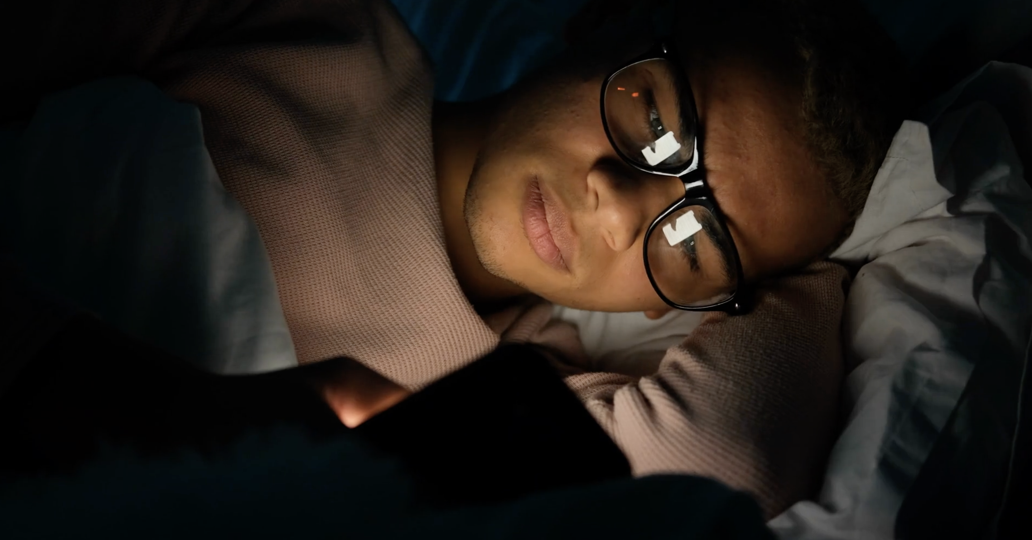 teenage boy lying in bed on his phone looking worried