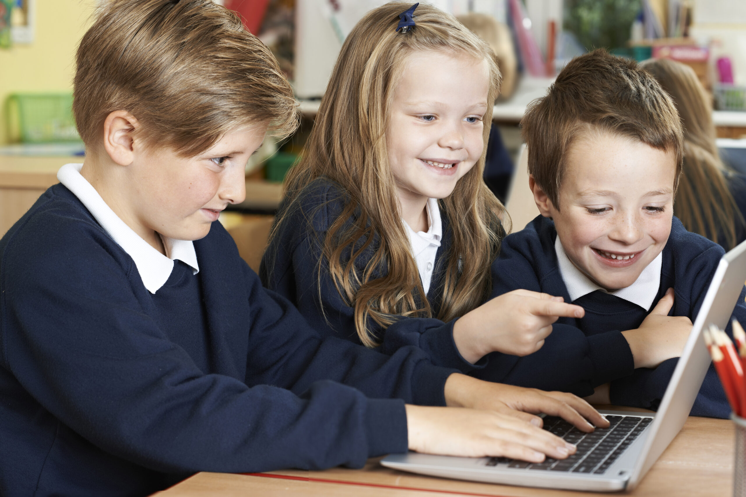 two young boys and a girl in school uniforms on a laptop