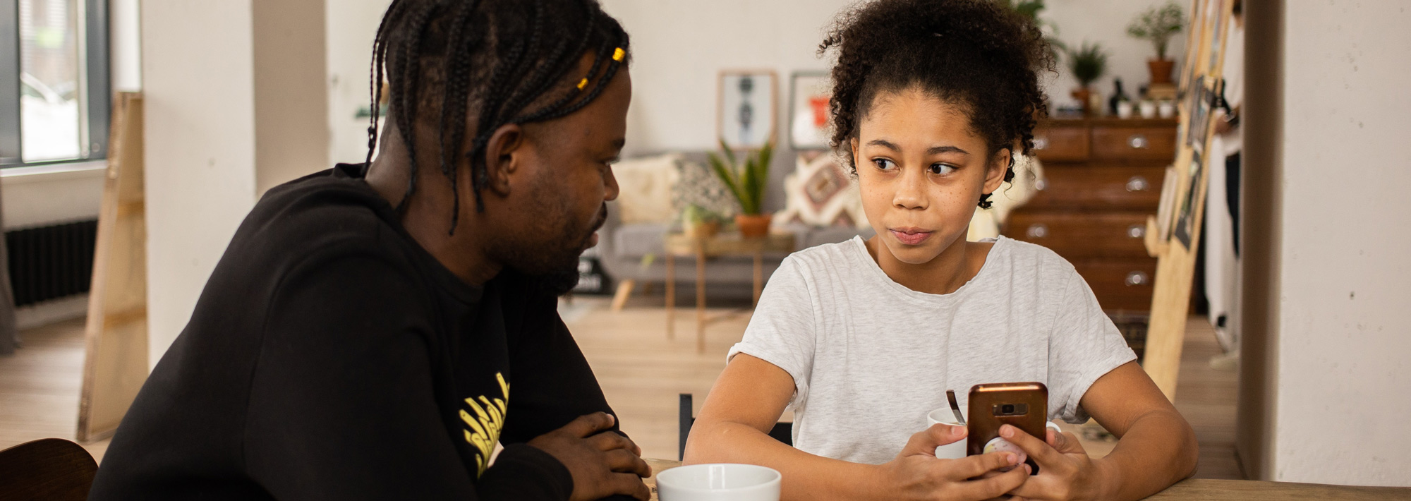 girl sat at the table on her phone whilst talking to her dad